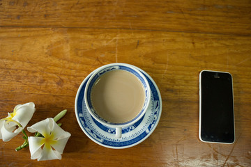 Plumeria flower, coffee cup and phone on the table