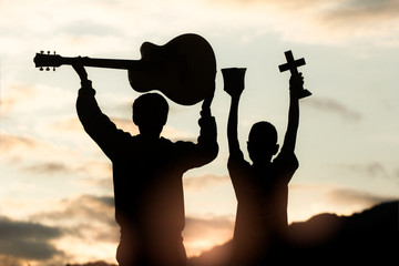 Two young christian worship God by holding cross and  with light sunset background,christian...