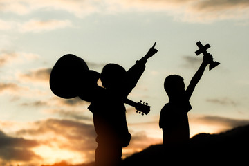 Two young christian holding cross and guitar on moutain with light sunset background,christian...