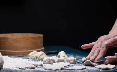 Female hands form pieces of dough on the table.