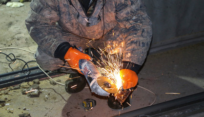  hands of the worker in gloves cut metal profile with a grinding machine. orange sparks fly from the grinding machine while cutting iron.