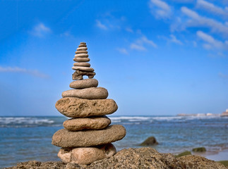 Fototapeta na wymiar balanced stone cairn on a rock in front of ocean and blue sky