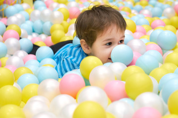 Fototapeta na wymiar child of three years old is playing in a ball pool. boy smiling spends fun time in the children's room