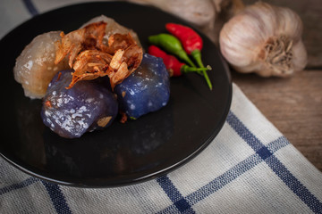 Sago pork in circle black plate with fried garlic toping have garlic place backside and chilli place on black plate on tablecloth and wood background