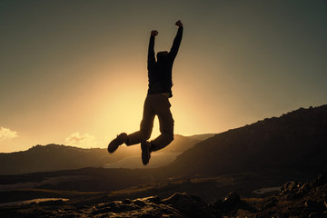 Courage man jumps on the top of mountain in sunset. Victory concept