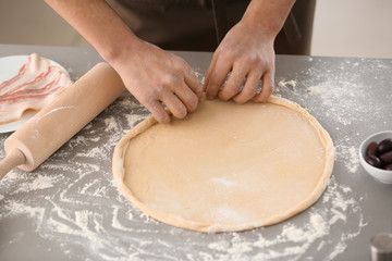 Obraz na płótnie Canvas Young man preparing dough for pizza at table