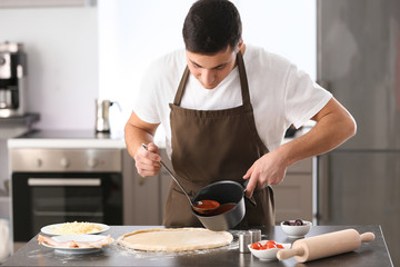 Young man applying sauce on pizza dough at table
