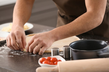 Young man preparing dough for pizza at table