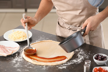 Young man applying sauce on pizza dough at table