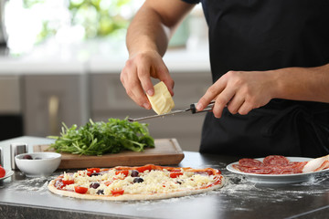 Young man preparing tasty pizza at table