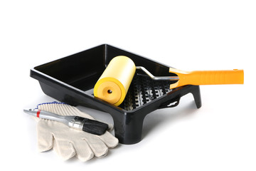 Paint roller in tray, brush and gloves on white background