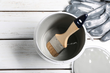 Paint can with brush and gloves on wooden table