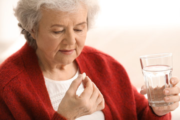Elderly woman taking pill on light background