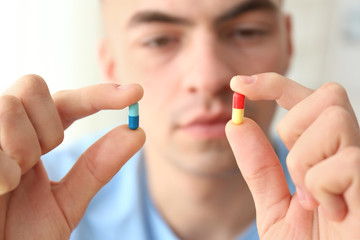 Young man holding different pills, closeup