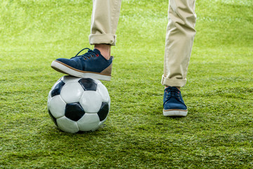 cropped view of boy with leg standing on soccer ball on lawn