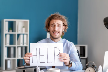 Stressed businessman with word HELP written on paper sheet. Deadline in office
