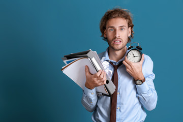 Stressed businessman trying to meet deadline on color background