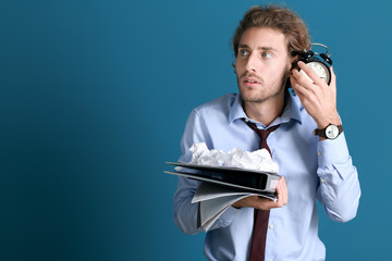 Stressed businessman trying to meet deadline on color background