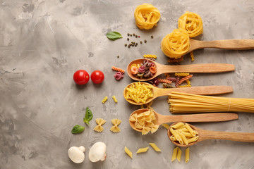 Fototapeta na wymiar Spoons with different types of raw pasta on grey background