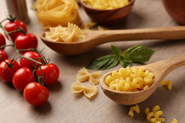 Spoons with raw pasta and tomatoes on wooden table