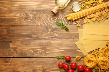 Different types of raw pasta with oil on wooden background