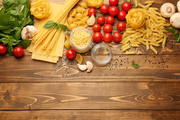 Different types of raw pasta with vegetables on wooden table