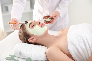 Obraz na płótnie Canvas Cosmetologist applying mask onto face of young woman in beauty salon