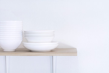 Wooden shelf template isolated on white wall background which on set stacked white bowls and plates as items tableware for decorated interior or montage of your product on shelf with copy space.