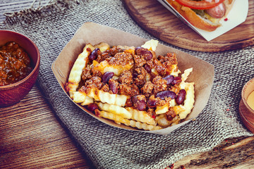 Close up view on traditional american fast food. French fries with bacon and salsa sauce on brown background. Copy space for text logo or brand.