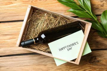 Bottle of wine in box with greeting card for Father's Day on wooden background