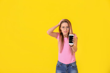 Emotional young woman with inoperable mobile phone on color background