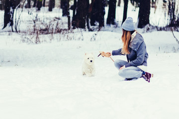 beautiful woman playing with a white Terrier in a snowy woods