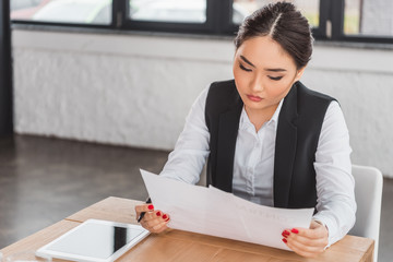 concentrated young asian businesswoman holding papers and working in office