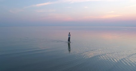 Beautiful dreaming woman walking in shallow reflecting sea water at sunset slow motion - Powered by Adobe