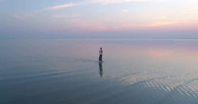 Beautiful dreaming woman walking in shallow reflecting sea water at sunset slow motion