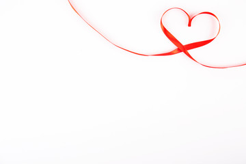 Isolated silk red ribbon laid in heart shape on bright white background. Festive decoration. Mother's, Women's, Wedding, Happy st Valentines Day concept, 14th February. Top view, flat lay, close up.