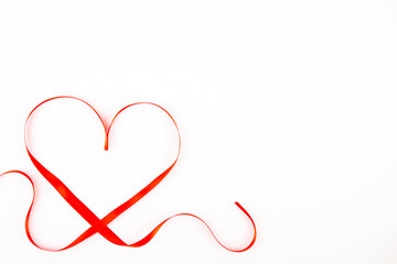 Isolated silk red ribbon laid in heart shape on bright white background. Festive decoration. Mother's, Women's, Wedding, Happy st Valentines Day concept, 14th February. Top view, flat lay, close up.