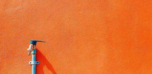Blue faucet or tap and water pipe installed on orange concrete wall with right copy space - Object, colorful background and Public utility concept 