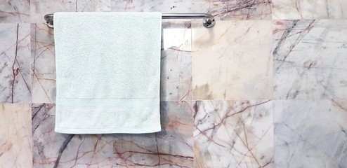 Light green towel or napkin hang on stainless steel hanger with white marble wall background in bathroom with copy space  - Cleaning, Shape and Surface of stone concept 