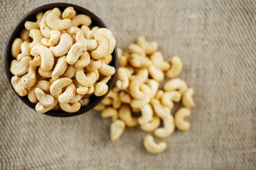 Cashew nuts in a wooden bowl on a burlap cloth background.