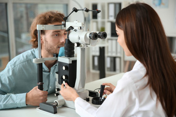 Ophthalmologist examining young man in clinic - obrazy, fototapety, plakaty