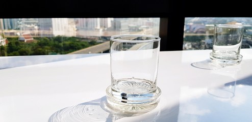 Close up clear glass of water on the white table and sunlight from side with window, cityscape view and transportation in the city background - Object and Art concept