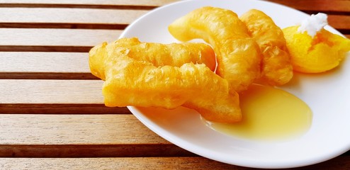 Deep-fried dough stick with sweet milk sauce in dish or plate on brown table with copy space 