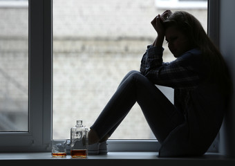 Depressed woman drinking alcohol near window