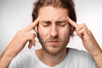 Young man suffering from headache on light background