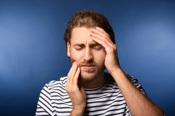 Young man suffering from headache on color background