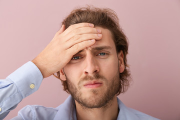 Young man suffering from headache on color background