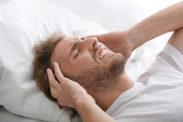 Fototapeta na wymiar Young man suffering from headache in bedroom