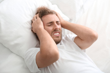 Young man suffering from headache in bedroom