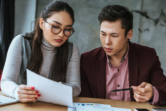 focused young asian business colleagues looking at papers in office